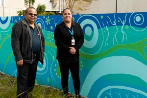 Two aboriginal people in front of aboriginal artwork